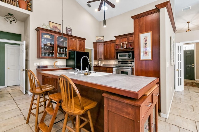 kitchen featuring a center island with sink, glass insert cabinets, appliances with stainless steel finishes, high vaulted ceiling, and a sink