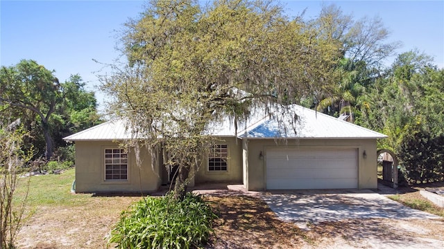 ranch-style home featuring a garage, driveway, metal roof, and stucco siding