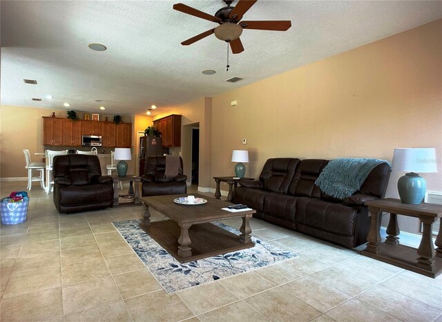 living room with ceiling fan, light tile patterned flooring, and a textured ceiling