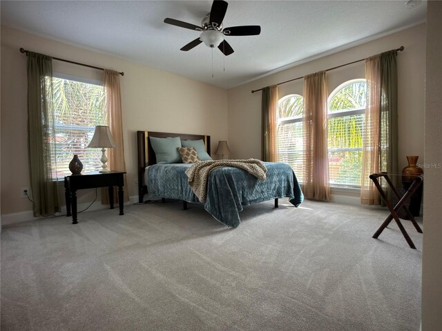 bedroom with ceiling fan, light colored carpet, and multiple windows