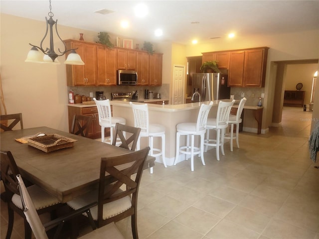 kitchen with hanging light fixtures, a chandelier, a kitchen bar, decorative backsplash, and appliances with stainless steel finishes