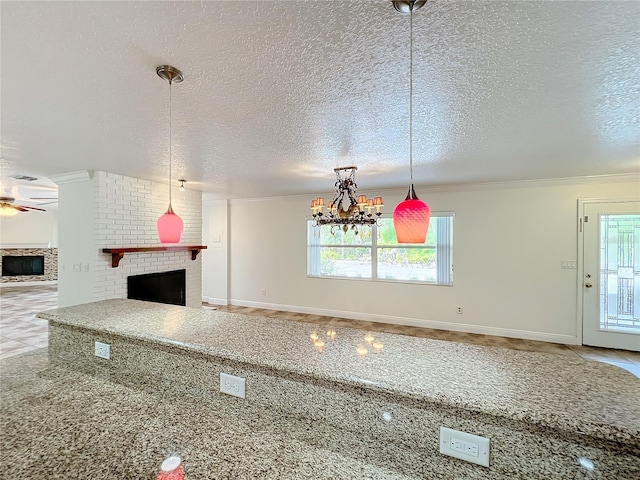 kitchen featuring a brick fireplace, a textured ceiling, decorative light fixtures, ceiling fan with notable chandelier, and ornamental molding