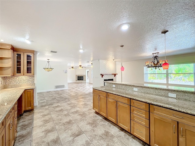 kitchen featuring light stone countertops, hanging light fixtures, ceiling fan with notable chandelier, and a brick fireplace