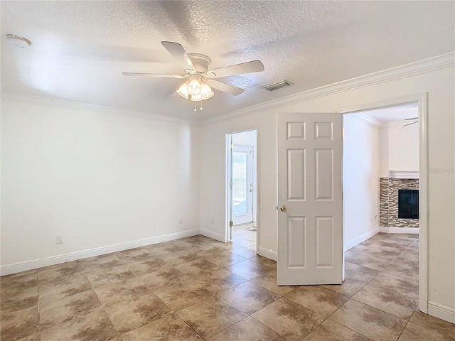 empty room featuring ceiling fan, a stone fireplace, ornamental molding, and a textured ceiling