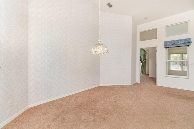 carpeted empty room with an inviting chandelier