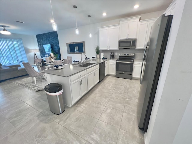 kitchen featuring open floor plan, a peninsula, hanging light fixtures, stainless steel appliances, and a sink