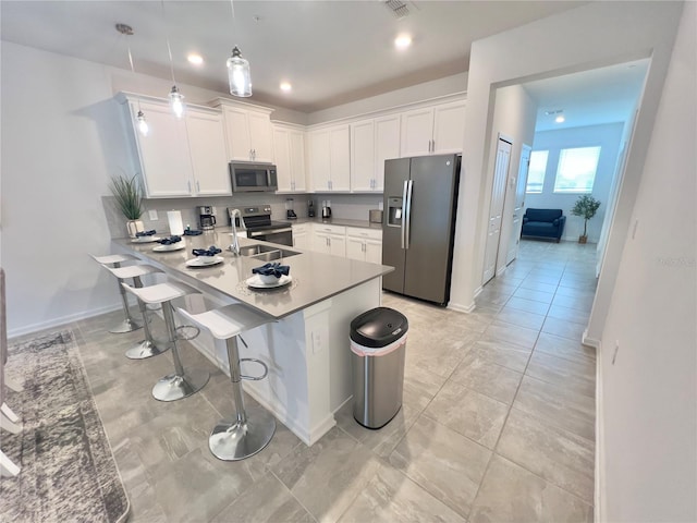 kitchen with appliances with stainless steel finishes, a breakfast bar area, decorative light fixtures, white cabinetry, and a sink