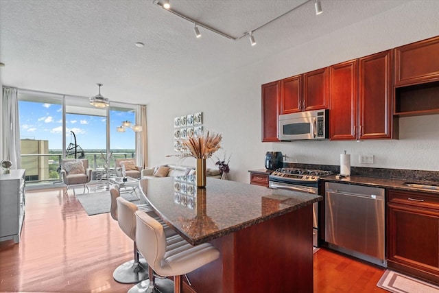 kitchen with dark hardwood / wood-style floors, stainless steel appliances, dark stone counters, and a center island