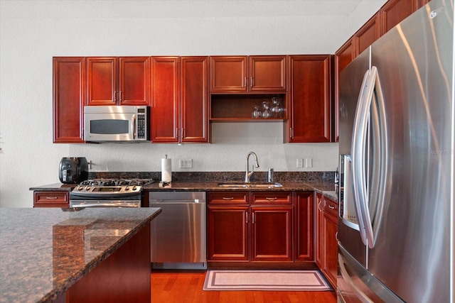 kitchen with appliances with stainless steel finishes, dark stone counters, dark wood-type flooring, and sink