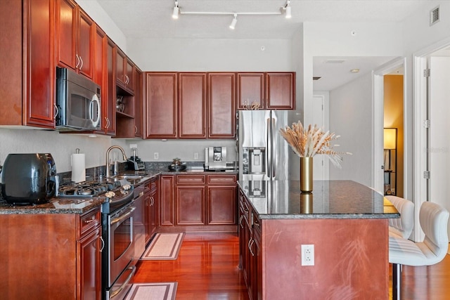 kitchen with sink, dark stone counters, dark hardwood / wood-style flooring, stainless steel appliances, and track lighting