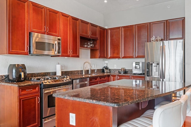 kitchen with sink, dark stone countertops, a breakfast bar area, stainless steel appliances, and a center island