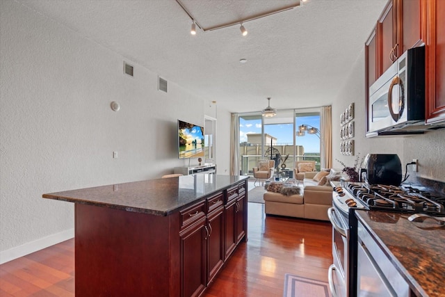 kitchen with a center island, dark stone counters, a textured ceiling, dark wood-type flooring, and appliances with stainless steel finishes