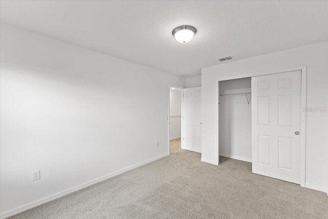 unfurnished bedroom with light carpet, a textured ceiling, and a closet