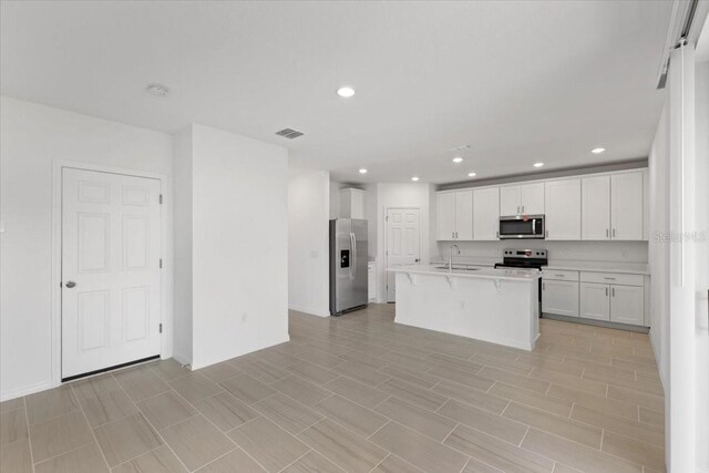 kitchen featuring sink, a center island with sink, stainless steel appliances, white cabinets, and a kitchen bar