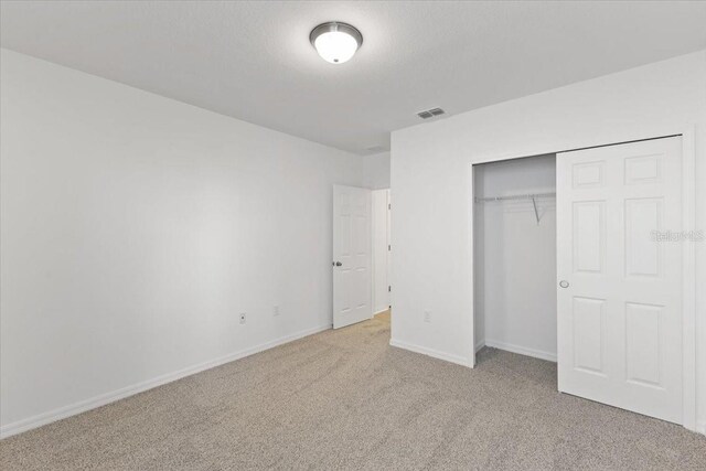 unfurnished bedroom with light carpet, a textured ceiling, and a closet