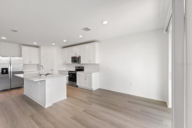 kitchen with a breakfast bar, appliances with stainless steel finishes, an island with sink, white cabinets, and decorative backsplash