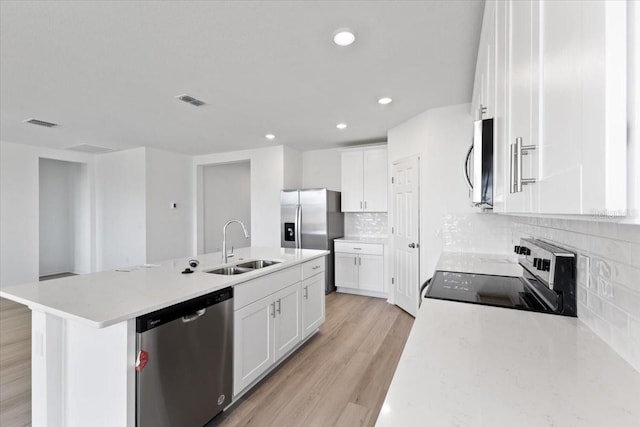 kitchen with appliances with stainless steel finishes, white cabinetry, an island with sink, sink, and light wood-type flooring