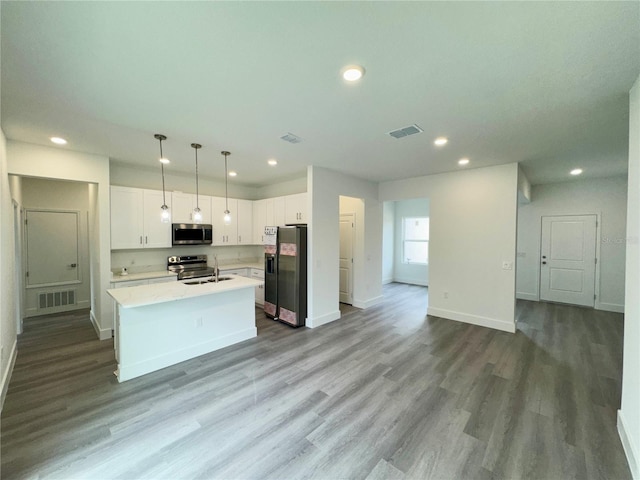 kitchen featuring appliances with stainless steel finishes, decorative light fixtures, white cabinets, light wood-type flooring, and a kitchen island with sink