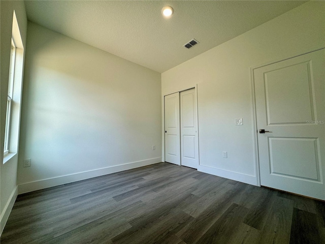 unfurnished bedroom featuring a closet, vaulted ceiling, dark hardwood / wood-style floors, and a textured ceiling