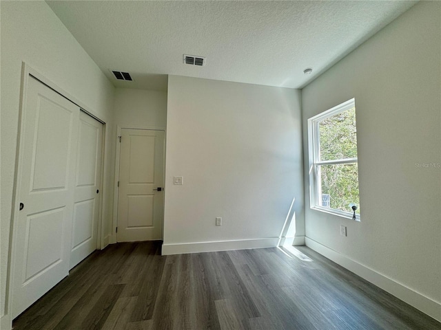 unfurnished bedroom with a textured ceiling, a closet, and dark hardwood / wood-style flooring