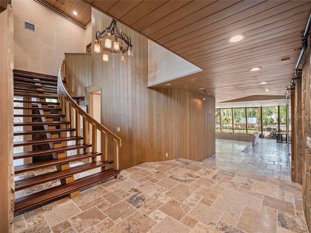 staircase with a notable chandelier, wooden ceiling, and wood walls