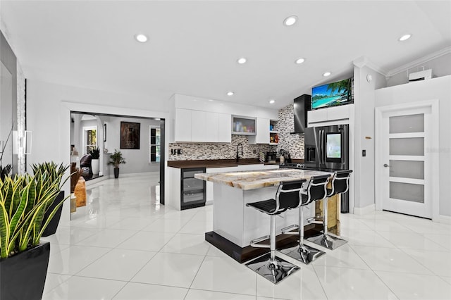 kitchen with sink, white cabinetry, a kitchen breakfast bar, a center island, and wine cooler