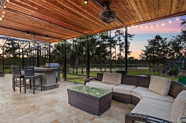 patio terrace at dusk featuring an outdoor kitchen, an outdoor hangout area, a playground, and an outdoor bar