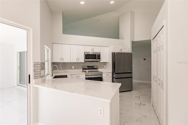 kitchen with sink, white cabinetry, light stone counters, appliances with stainless steel finishes, and kitchen peninsula