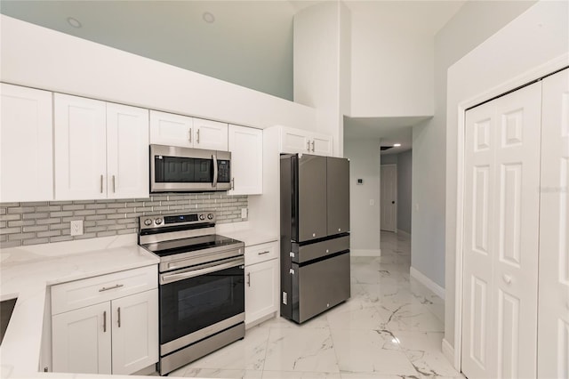 kitchen featuring white cabinetry, a towering ceiling, appliances with stainless steel finishes, and light stone countertops