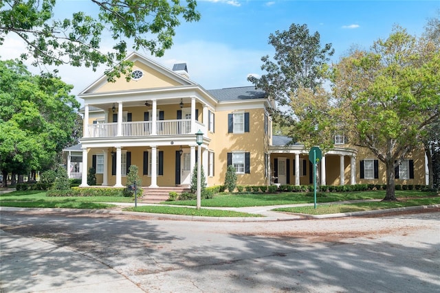 greek revival house with a front lawn, a balcony, and covered porch