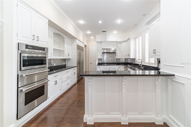 kitchen with dark hardwood / wood-style floors, kitchen peninsula, crown molding, white cabinets, and backsplash