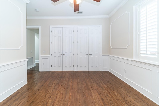 unfurnished bedroom featuring dark hardwood / wood-style flooring, ceiling fan, ornamental molding, and multiple closets