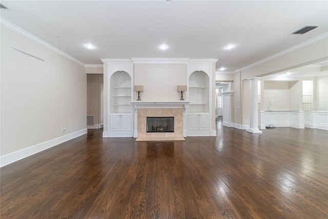 unfurnished living room with dark hardwood / wood-style floors, built in shelves, a premium fireplace, ornamental molding, and ornate columns