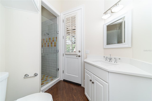 bathroom with toilet, a tile shower, wood-type flooring, and vanity