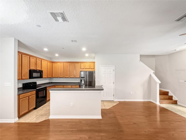 kitchen with a textured ceiling, a kitchen island with sink, light tile floors, and black appliances