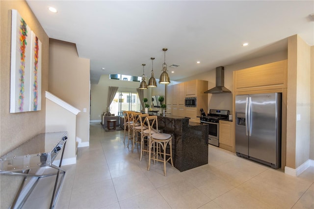 kitchen featuring appliances with stainless steel finishes, wall chimney range hood, a center island with sink, and light tile floors