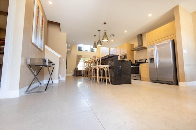 kitchen featuring appliances with stainless steel finishes, hanging light fixtures, a high ceiling, wall chimney range hood, and a breakfast bar