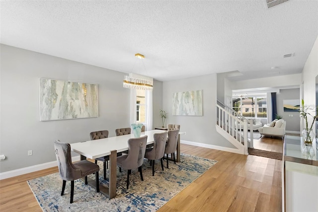 dining room featuring ceiling fan with notable chandelier, a textured ceiling, and light wood-type flooring