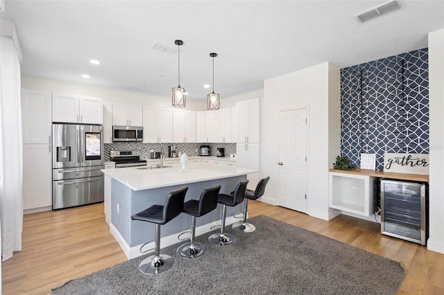 kitchen with appliances with stainless steel finishes, a center island with sink, light hardwood / wood-style floors, tasteful backsplash, and wine cooler