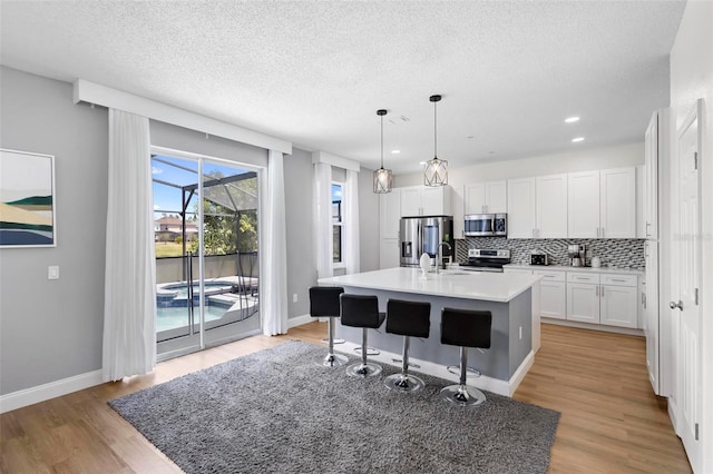 kitchen featuring light hardwood / wood-style floors, white cabinetry, decorative light fixtures, stainless steel appliances, and an island with sink