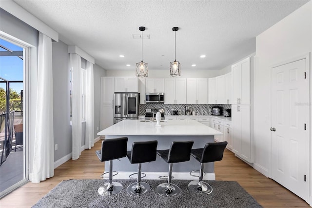 kitchen with light hardwood / wood-style flooring, stainless steel appliances, and a center island with sink