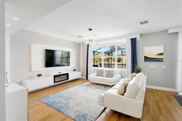 living room with light hardwood / wood-style flooring, a notable chandelier, and a textured ceiling