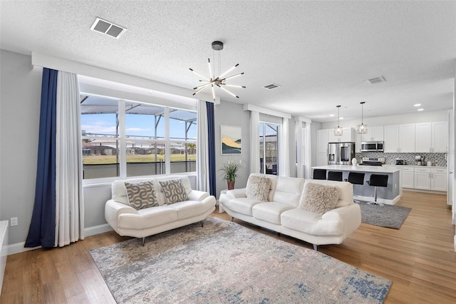 living room featuring sink, an inviting chandelier, a textured ceiling, and light wood-type flooring