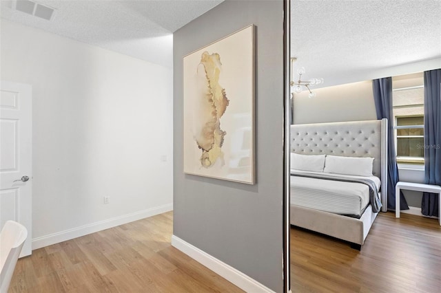 bedroom with hardwood / wood-style flooring, an inviting chandelier, and a textured ceiling