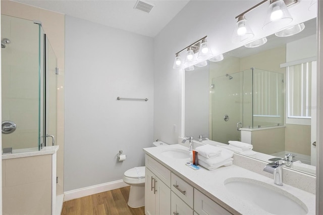 bathroom featuring a shower with shower door, toilet, hardwood / wood-style flooring, and double sink vanity