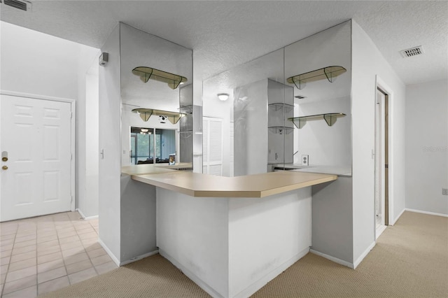 kitchen featuring light carpet, a textured ceiling, and kitchen peninsula