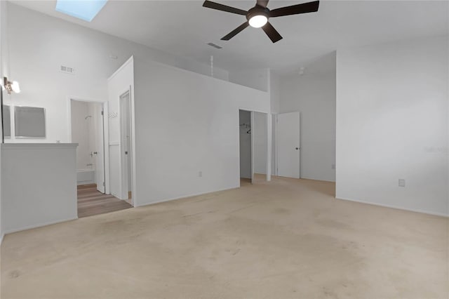 carpeted spare room with high vaulted ceiling, a skylight, and ceiling fan