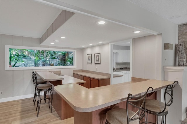 kitchen with a spacious island, white cabinetry, a textured ceiling, a kitchen bar, and light hardwood / wood-style floors