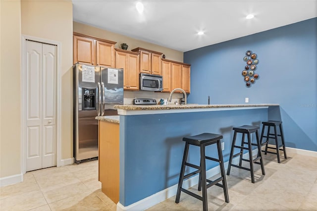 kitchen with a kitchen breakfast bar, light tile flooring, appliances with stainless steel finishes, light stone counters, and sink