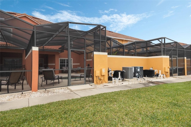 rear view of property with central AC unit, a patio, a yard, and glass enclosure